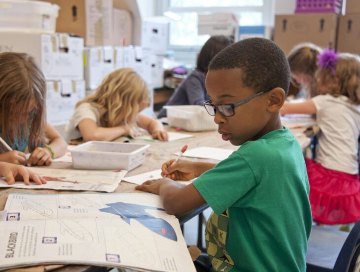 students in a classroom sitting at desks and working on a textbook assignment